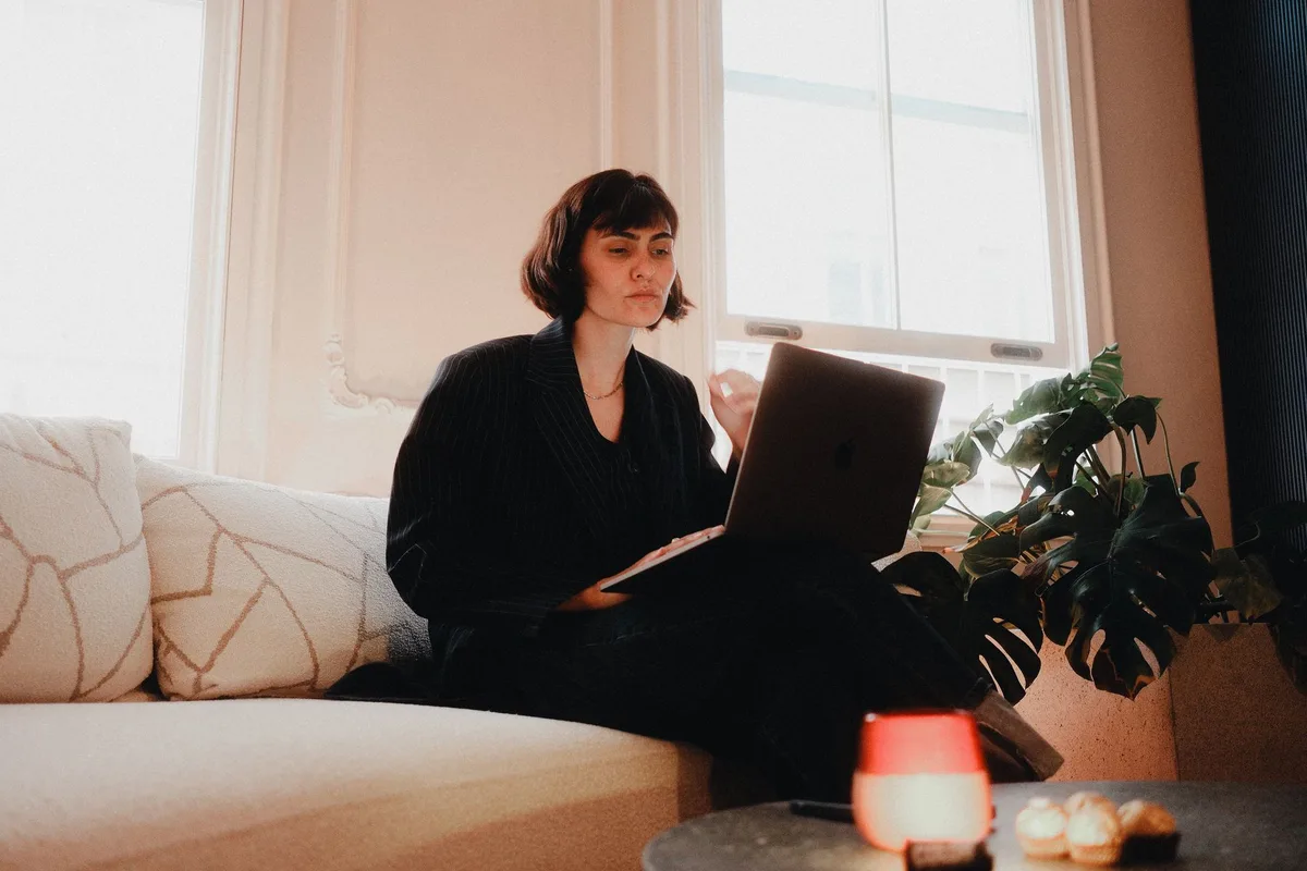 Person working online on a laptop at a wooden desk with a notepad