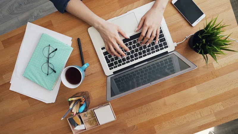 Person typing on a laptop with a notebook and coffee nearby