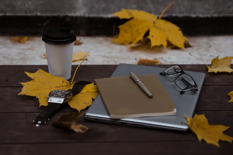Writer working at a cozy desk with notebook and laptop in autumn workspace