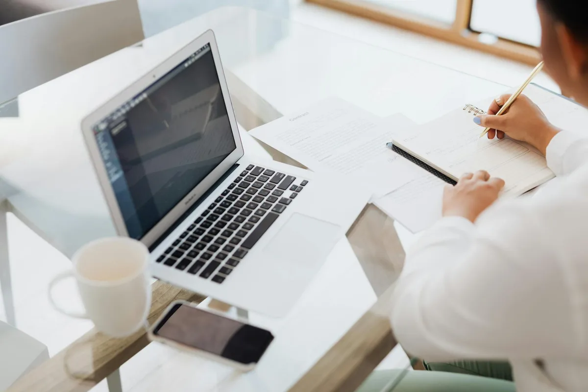 A creator working at a laptop with notebooks and a cup of coffee, planning a digital product business