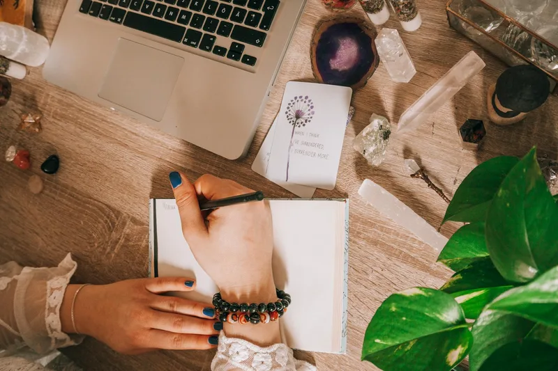 A person at a desk writing in a journal surrounded by plants, representing creative and reflective digital product content