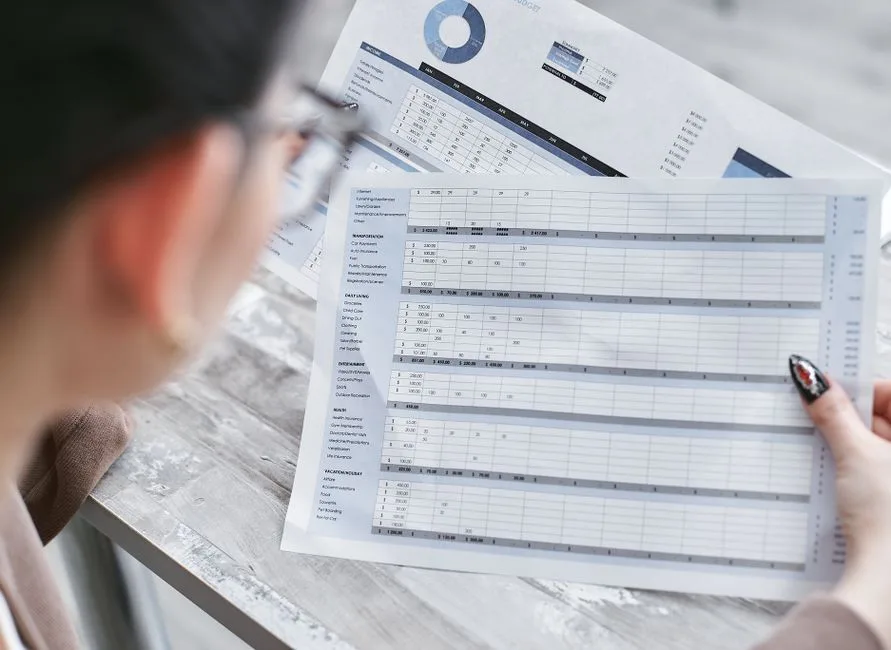A businesswoman reviewing financial spreadsheets with charts and graphs, comparing platform costs