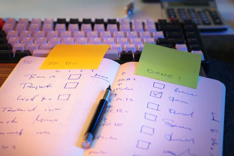 Open notebook with a handwritten checklist, a yellow To Do note and a green Done note, next to a keyboard