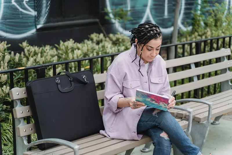 Artist sitting outdoors reviewing and sketching in a portfolio