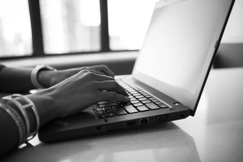Close-up black-and-white photo of hands typing on a laptop keyboard
