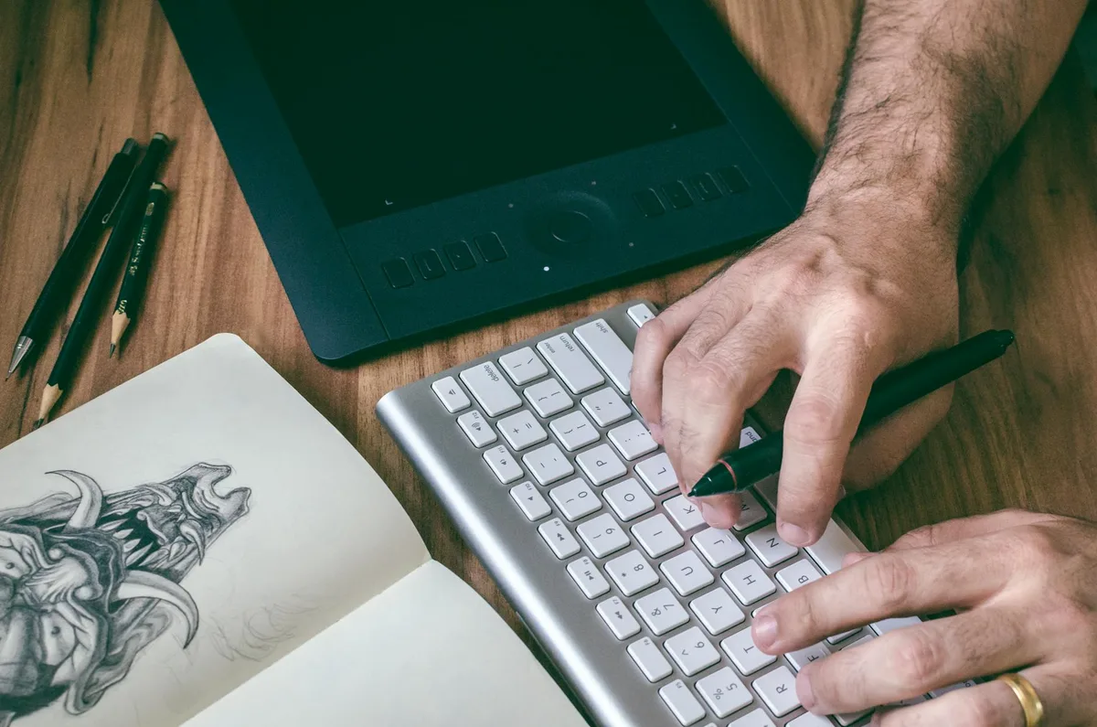 An artist digitizing artwork at a desk with a scanner and computer