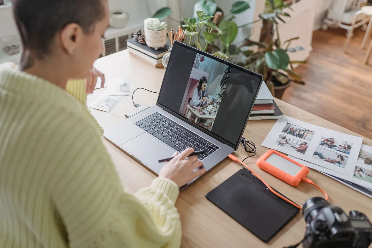 Photographer editing stock photos on a laptop with a graphics tablet at a home workspace