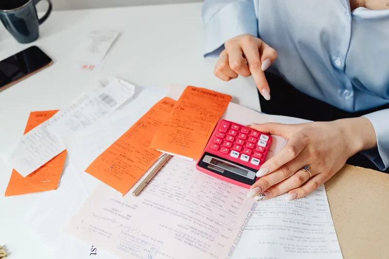 Person calculating expenses with a calculator and paper receipts for bookkeeping