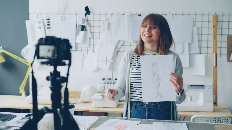Fashion designer filming herself presenting a sketch on camera in a studio setup